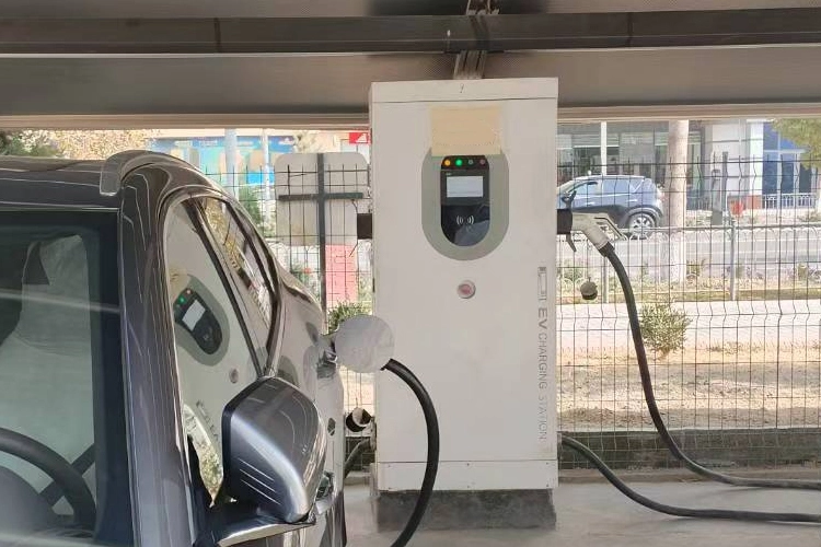 Electric vehicle charging station in Kazakhstan, showing a car connected to a DC fast charger under a covered parking area.